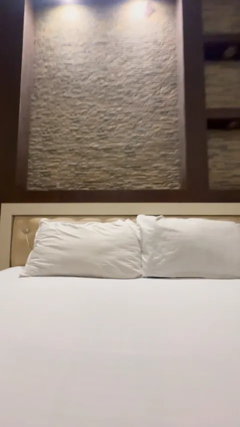White bedding below a textured feature wall and reading lights at Hotel Max